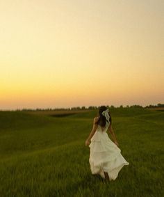 a woman in a white dress is walking through the grass at sunset with her back to the camera