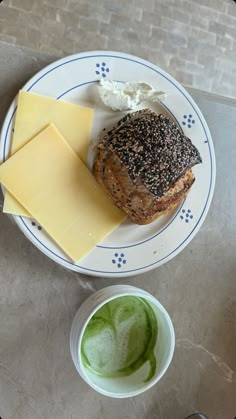 a white plate topped with bread and cheese next to a cup of green liquid on top of a table