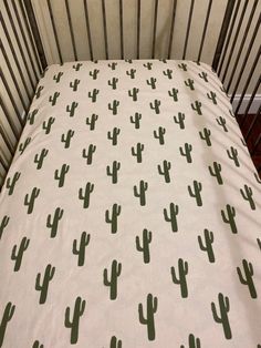 a crib with a white sheet and green cactus print on it's side