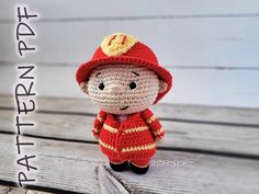 a small crocheted stuffed animal wearing a red hat and jacket, standing on a wooden surface