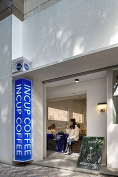 people are sitting at the entrance to a coffee shop with large blue sign in front of it