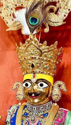 an elaborately decorated mask with feathers on it's head is displayed in front of a red background