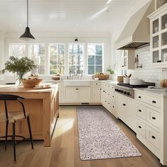 a large kitchen with white cabinets and wooden flooring, along with an area rug on the floor