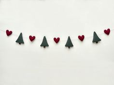 red and green christmas trees are hanging on a white string with heart - shaped pins