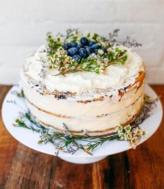 a cake with white frosting and blueberries on top sitting on a wooden table