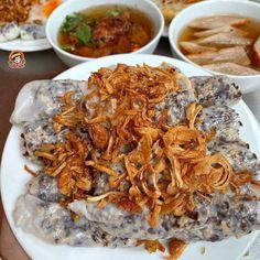 a white plate topped with meat covered in gravy next to bowls of soup