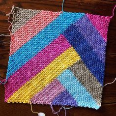 a multicolored crocheted square with yarn and thread on a wooden surface