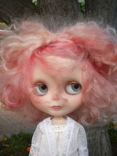 a doll with pink hair is standing in front of a tree and looking at the camera