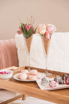 two champagne flutes with flowers in them on a tray next to plates and desserts