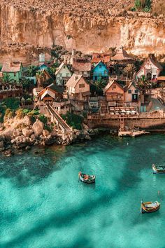 several small boats floating in the clear blue water next to a rocky cliff side village