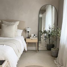 a white bed sitting next to a tall mirror in a bedroom under a light fixture