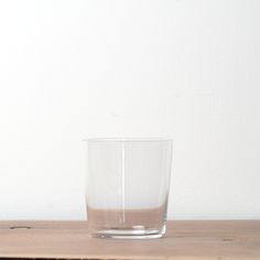 an empty glass sitting on top of a wooden table next to a white wall,