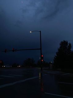 a traffic light sitting on the side of a wet road at night with clouds in the sky