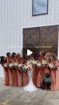 a group of women standing next to each other in front of a barn door holding bouquets