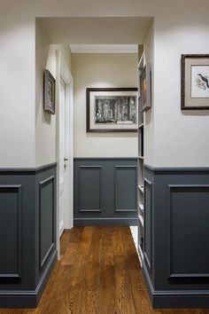 an empty hallway with wood flooring and gray painted trim on the walls, along with framed pictures