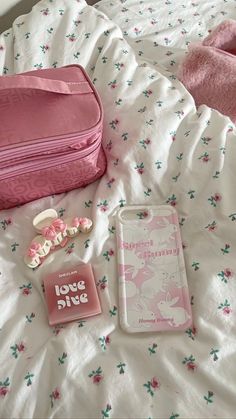 a pink suitcase sitting on top of a bed next to a book and other items