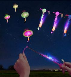 a person is holding a light up wand in front of some flying objects at night