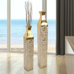 two gold vases sitting next to each other on a wooden floor in front of a window