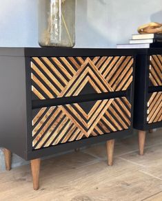 a black and wood dresser with geometric designs on the drawers, next to a vase filled with flowers