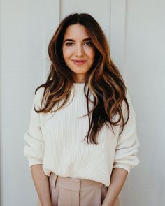 a woman standing in front of a white wall with her hands on her hips and smiling