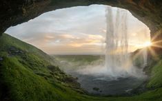 the sun shines through an opening in a cave with water spewing from it