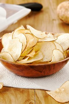 a wooden bowl filled with potato chips on top of a white napkin next to a knife