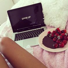 a laptop computer sitting on top of a bed next to a plate of berries and chocolate