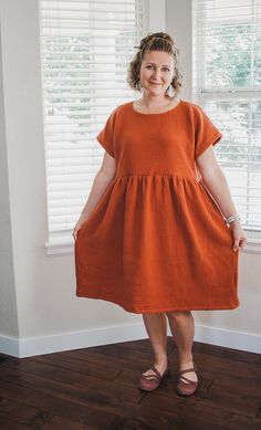 a woman standing in front of a window with her hands on her hips, wearing an orange dress