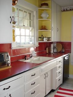 a kitchen with red counter tops and white cabinets, along with a striped rug on the floor