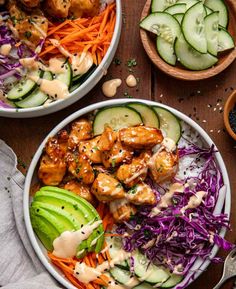 two bowls filled with chicken and veggies on top of a wooden table next to cucumbers