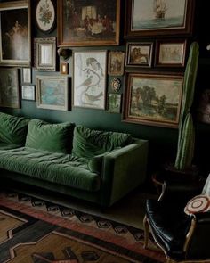 a green couch sitting in front of a wall covered with pictures and paintings on it