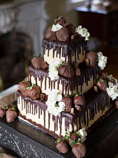 a triple layer cake with chocolate and strawberries on the top is decorated with white flowers