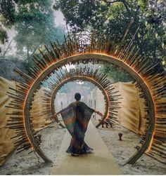 a woman is standing in front of a circular sculpture made out of sticks and wood