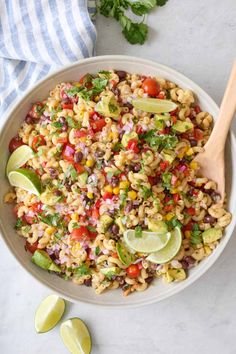 a white bowl filled with mexican rice salad next to limes and cilantro