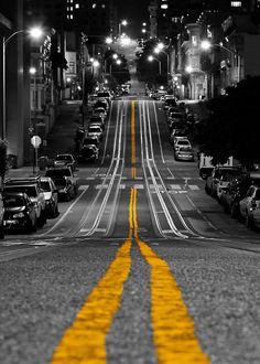 an empty city street at night with cars parked on both sides and yellow lines painted on the road