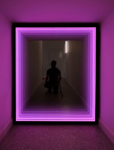 a person sitting on a chair in a room with purple light at the end of it