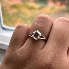 a person's hand with a diamond ring on their finger, next to a window