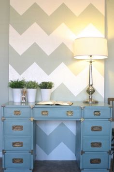 a blue desk with two potted plants and a book on it in front of a chevron wall