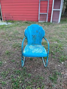 an old blue chair sitting in the grass near a red barn and shed with windows