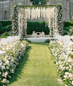 an outdoor ceremony setup with white flowers and greenery on the lawn, surrounded by tall hedges