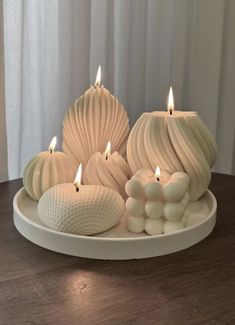 some white candles sitting on top of a plate with rocks and shells around them in the shape of seashells