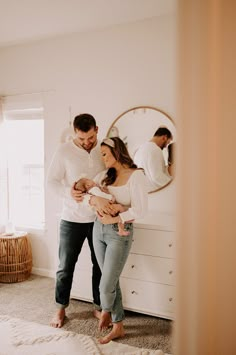 a man and woman standing in front of a mirror holding their newborn son, who is looking at his belly