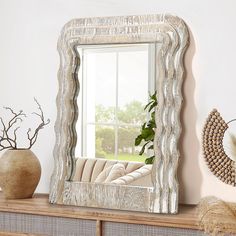 a mirror sitting on top of a dresser next to a vase and potted plant