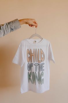 SIZE RESTOCK IS COMING SOON.  You are a Child of the King! This shirt is based off the verse "We are all children of God by faith in Christ Jesus"- Galatians 3:26. This shirt in classic white is now available in sizes ranging from 0-3 months to kids XL. Let your little ones make a stylish statement with these cool and trendy Christian shirts that are perfect for any occasion. Help your kids showcase their faith and be reminded that they are a child of the King. All of God's promises are for them Christian Kids Shirts, Church Shirt, God's Promises, Christian Kids, Child Of God, Child Jesus, Christian Shirt, Mesa Az, Jesus Shirts