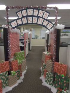 an office cubicle decorated for christmas with presents on the floor and santa's workshop sign