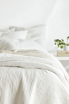 an unmade bed with white sheets, pillows and plants on the side table next to it