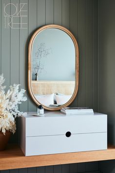 a white dresser with a mirror and flowers on it in front of a wooden shelf