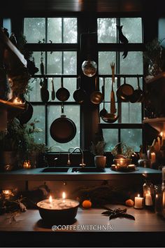 candles are lit in front of a kitchen window with pots and pans on it