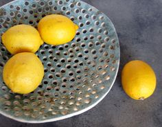 four lemons in a metal strainer bowl