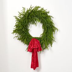 a green wreath with red tassels hanging on a wall next to a white wall